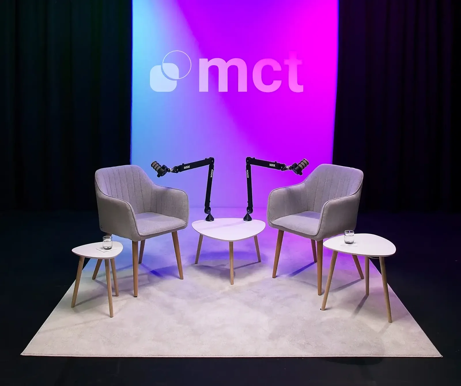 Cenário de podcast no estúdio: duas poltronas, microfones em braço e o logótipo da MCT iluminado a azul e rosa